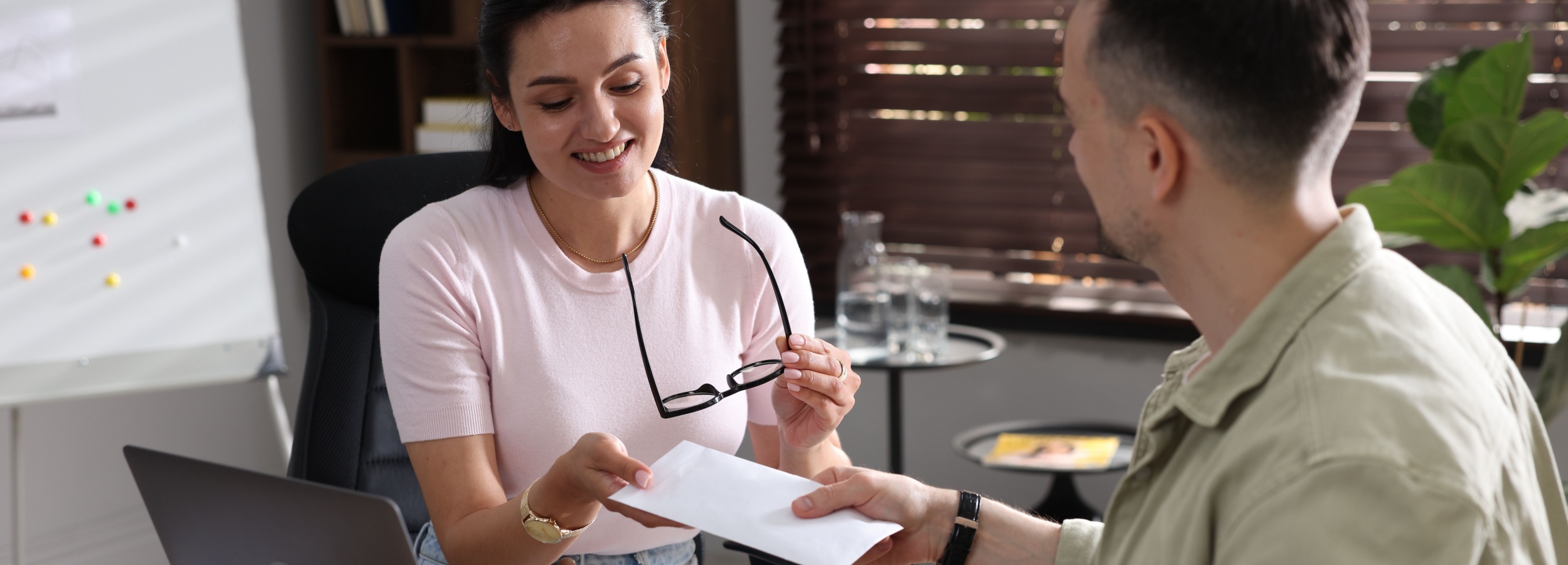 Mann gibt Umschlag mit Geld an eine Angestellte im Büro.