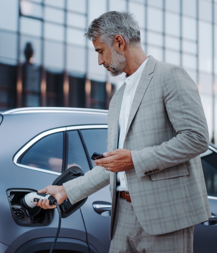 Mann in grauem Anzug hält das Ladekabel eines e-Autos an der Ladesäule, um sein Auto aufzuladen.